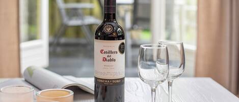 Una botella de vino Merlot Casillero del Diablo, dos copas de vino vacías y tres candelabros sobre una mesa.
