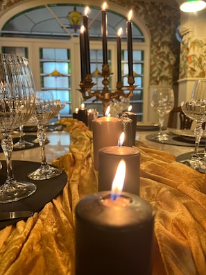 A dining table set with candles, glasses, and a golden drape.