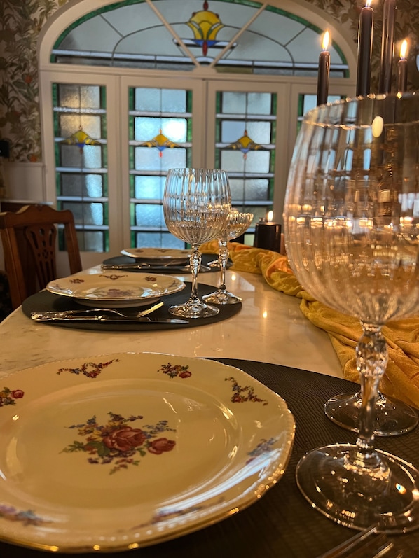 A dining table set with plates, cutlery, and wine glasses, with a stained glass window in the background.