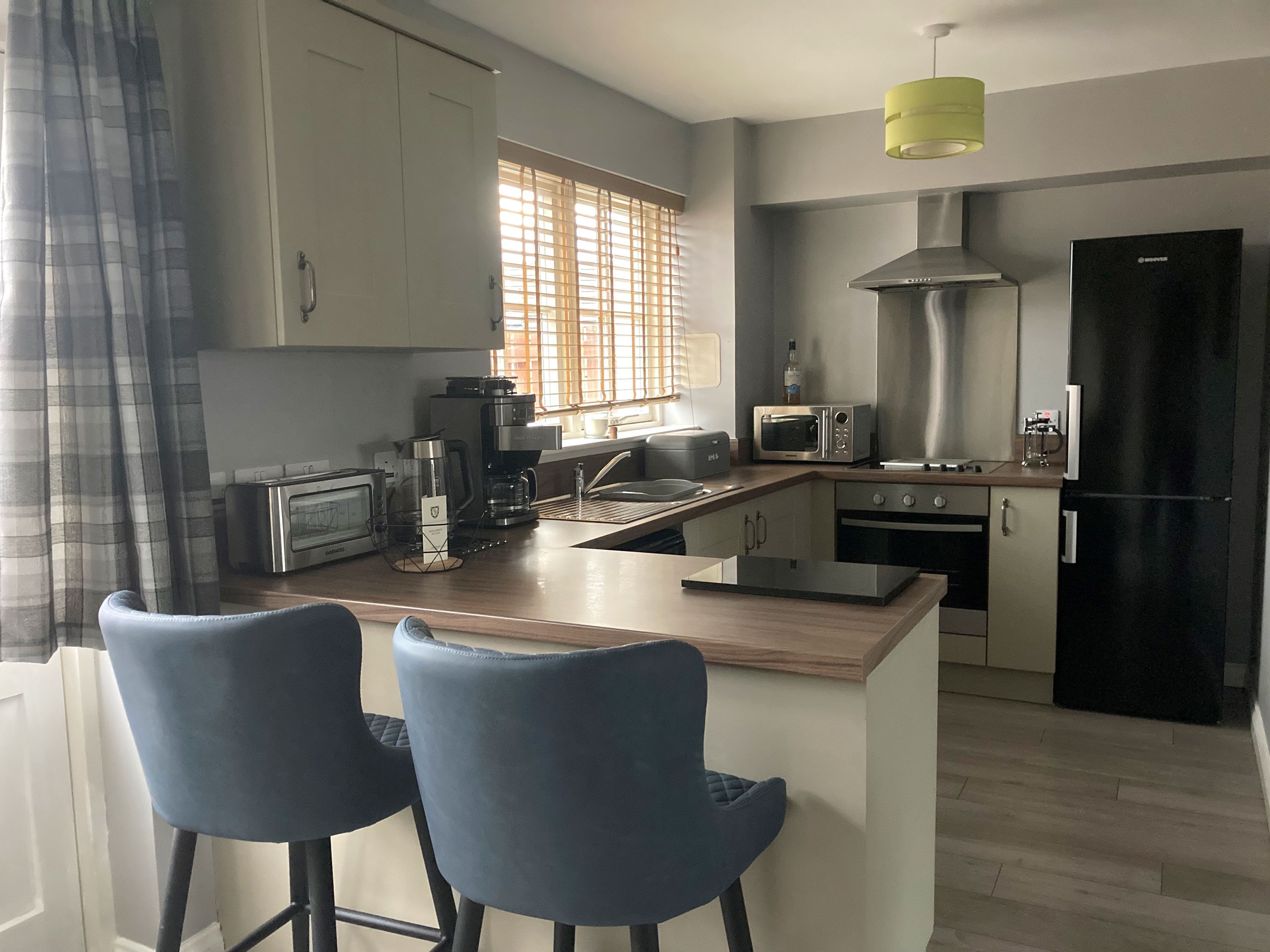 Una cocina moderna con una isla central, dos taburetes de bar, un microondas, una cafetera y un refrigerador.