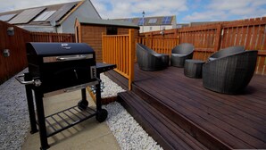 Ein Garten mit Grill, Korbstühlen, einer Holzterrasse und einem Holzzaun.
