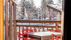 Eine Holzterrasse mit einem Tisch und roten Stühlen, mit Blick auf eine verschneite Landschaft mit Bäumen und Flaggen.