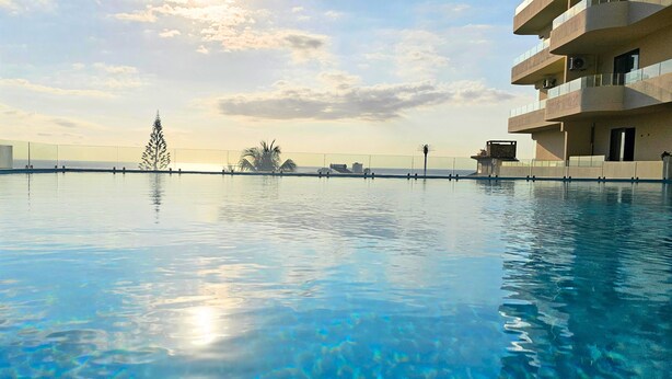 Ein klares Schwimmbecken mit Blick auf das Meer und ein Gebäude mit Balkonen.