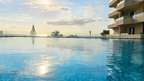 A clear swimming pool with a view of the sea and a building with balconies. - Zen Retreat with Stunning Sea Views and Sunsets, plus Common Pool and Gym Access (Flic en Flac)