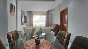 Ein modernes Hotelzimmer mit einem Glastisch, bequemen Sitzgelegenheiten, einem großen Fenster mit Aussicht und einer Holztür.