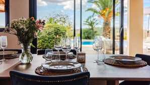 Une table à manger dressée avec des assiettes, des verres et un vase de fleurs, donnant sur une piscine et une végétation luxuriante.