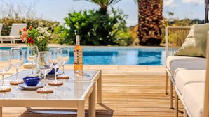Un espace aménagé au bord de la piscine, avec une table dressée pour les repas, un canapé et un palmier en arrière-plan.