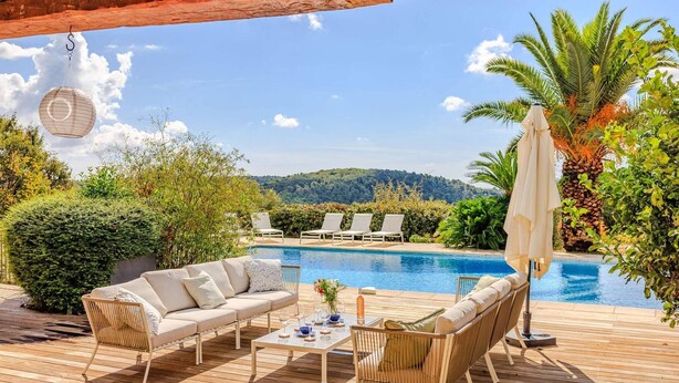 Un espace aménagé au bord de la piscine, avec une terrasse en bois, un canapé, des chaises longues et une table où sont servis des boissons.