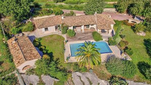 Une grande villa dotée d’une piscine, entourée d’une végétation luxuriante et accessible par un chemin de pierre.