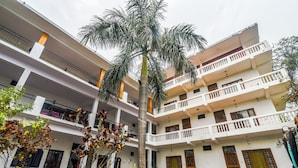Un edificio residencial de varios pisos con balcones, una palmera y una cerca blanca.