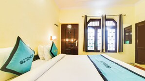 Habitación de hotel con cama, almohadas, mesita de noche, lámpara de pared y ventana con cortinas.