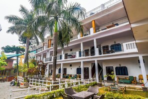 A multi-story building with balconies, outdoor seating, and palm trees. - Oscenox Swiss Cottage (Rishikesh)