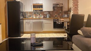 A modern kitchen with white cabinets, a black refrigerator, a coffee machine, and a glass table with a remote control. - Whitworth Street Apartment in Manchester (Manchester)