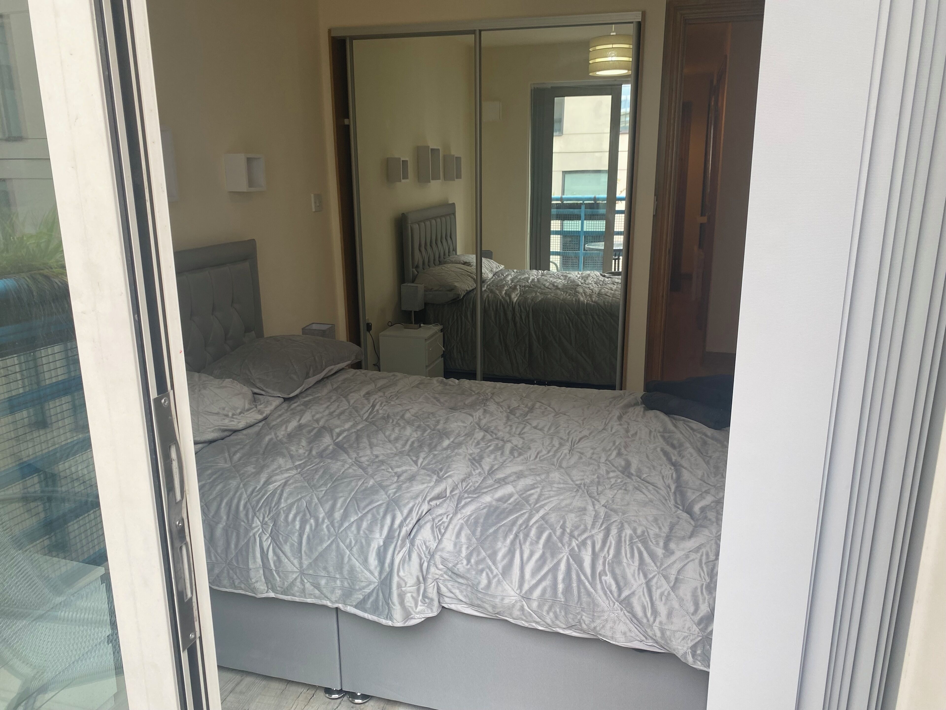 A bedroom with a bed, a nightstand, a mirror, and a door.
