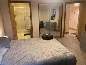 Una camera da letto con un letto, uno specchio, un armadio e un bagno con doccia e WC.