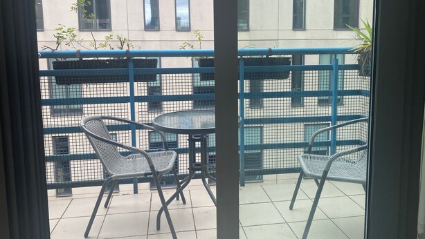 A balcony with two metal chairs and a small round table, overlooking a building with multiple windows. - Whitworth Street Apartment in Manchester (Manchester)