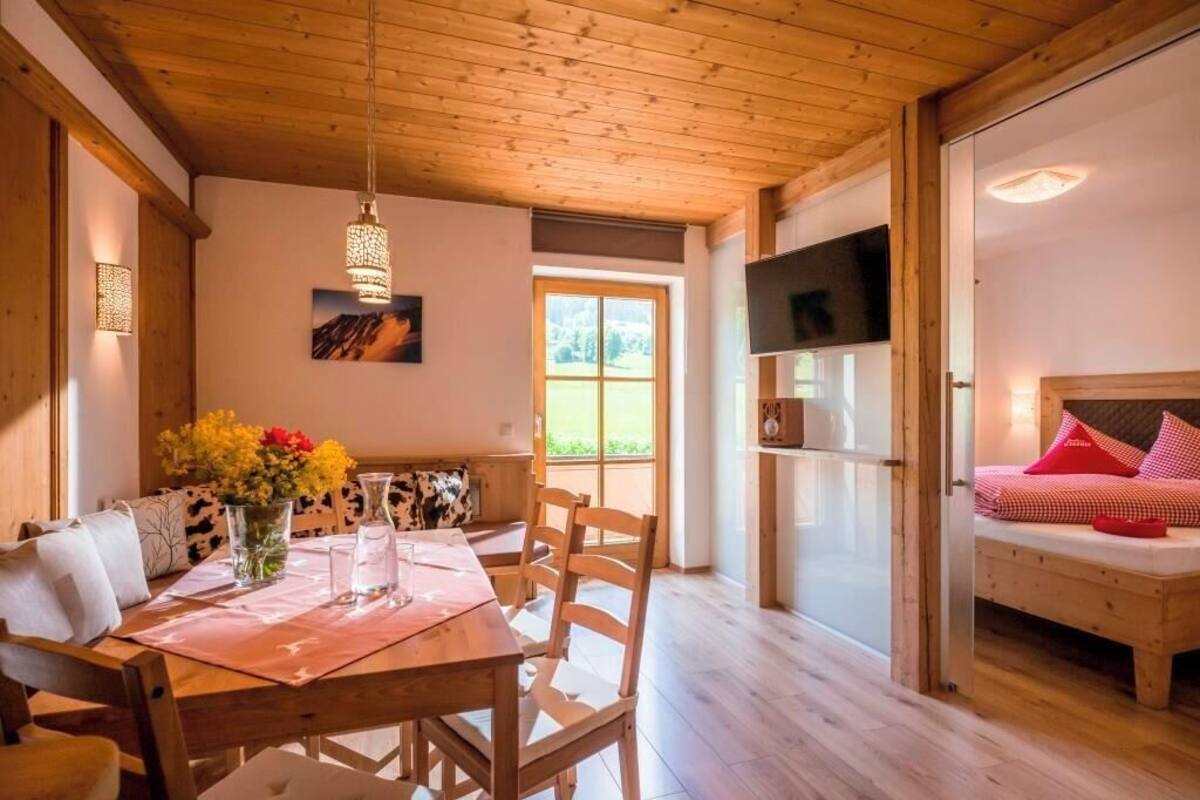 A wooden dining table with chairs, a vase of flowers, and a painting on the wall.