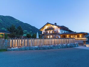 A two-story mountain lodge with a wooden fence and stone wall, featuring balconies and warm lighting. - Grittlmühle Chalet Ferienwohnungen (Brixen im Thale)