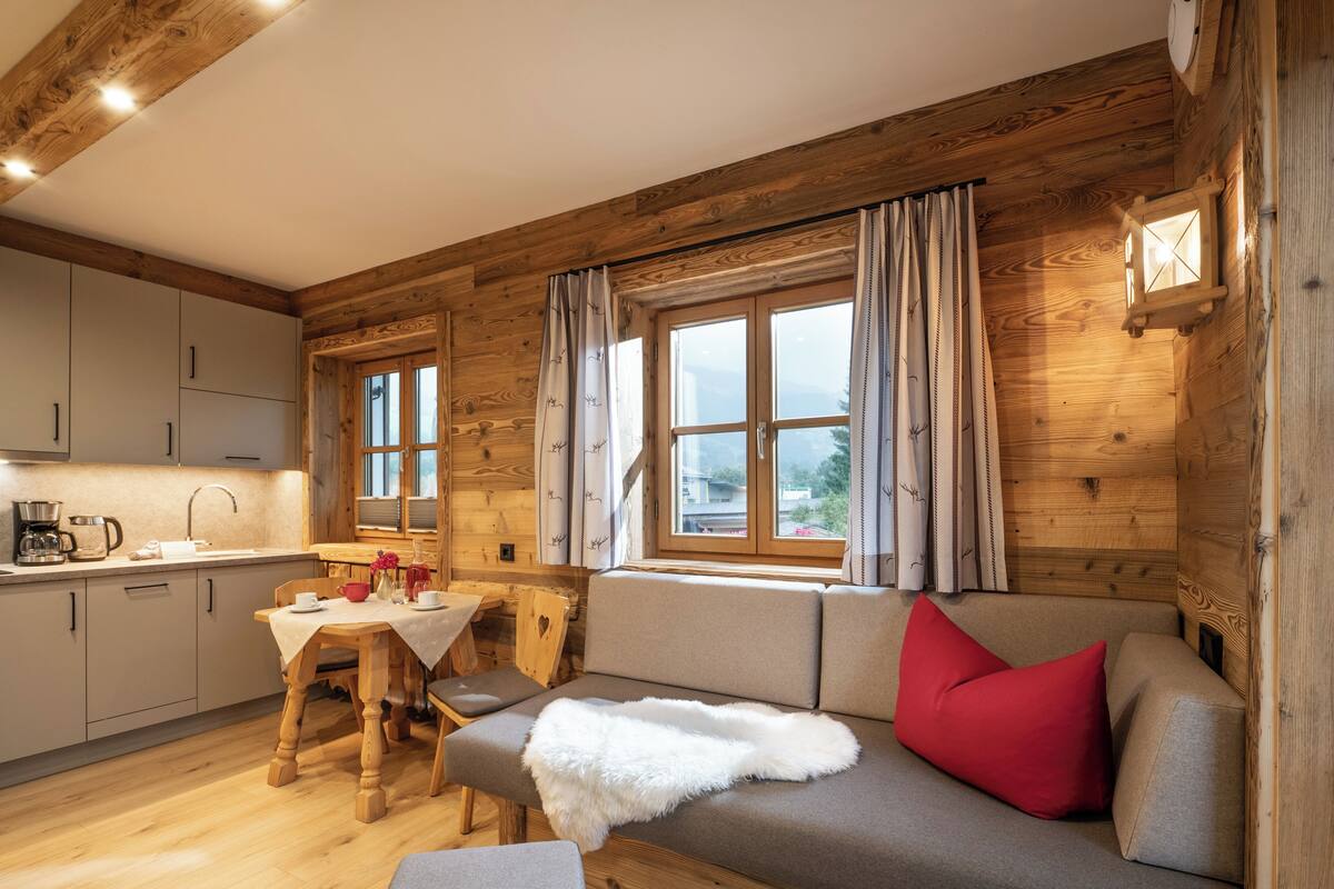 A cozy cabin-style room with a wooden interior, a dining area, and a sofa with a red pillow.