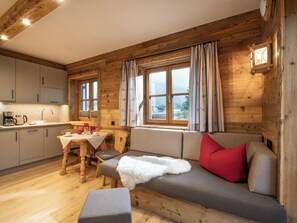 A cozy cabin-style room with a wooden interior, a dining area, and a sofa with a red pillow. - Grittlmühle Chalet Ferienwohnungen (Brixen im Thale)