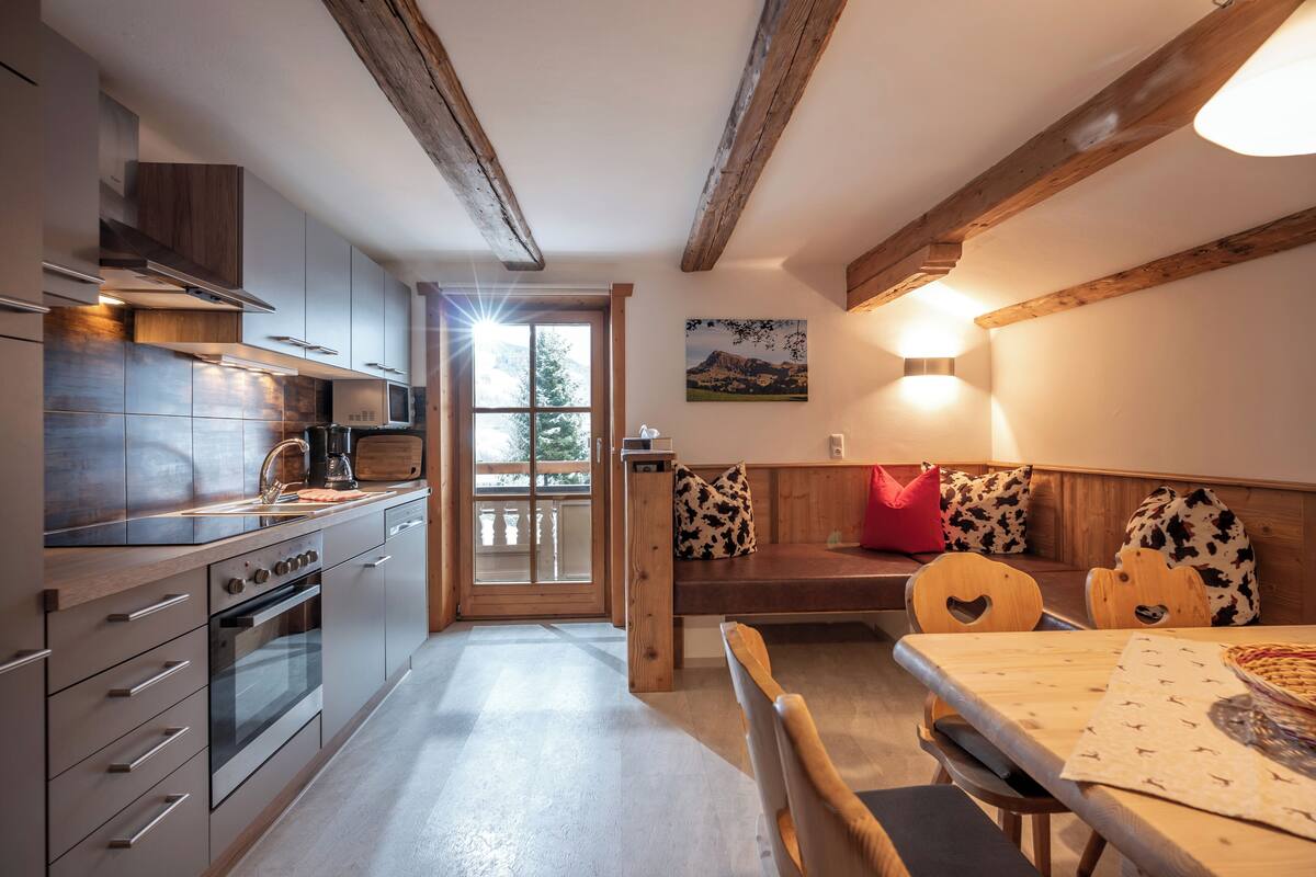 A modern kitchen with wooden beams, a dining area with a wooden table and chairs, and a bench with cow-print cushions.