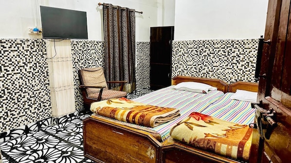 A bedroom with a bed, a chair, a television, and a wardrobe. - Hotel Nilamber By GRB (Lanka)