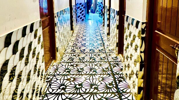 Un pasillo con baldosas de diseño, puertas de madera y techo iluminado en azul.