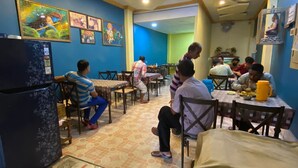 Un restaurante con paredes azules, ventiladores de techo y obras de arte. Mesas y sillas dispuestas para comer.