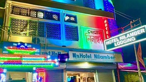 Un edificio de varios pisos con luces de neón de colores, un letrero que dice 'M/s Hotel Nilamber' y motocicletas estacionadas afuera.