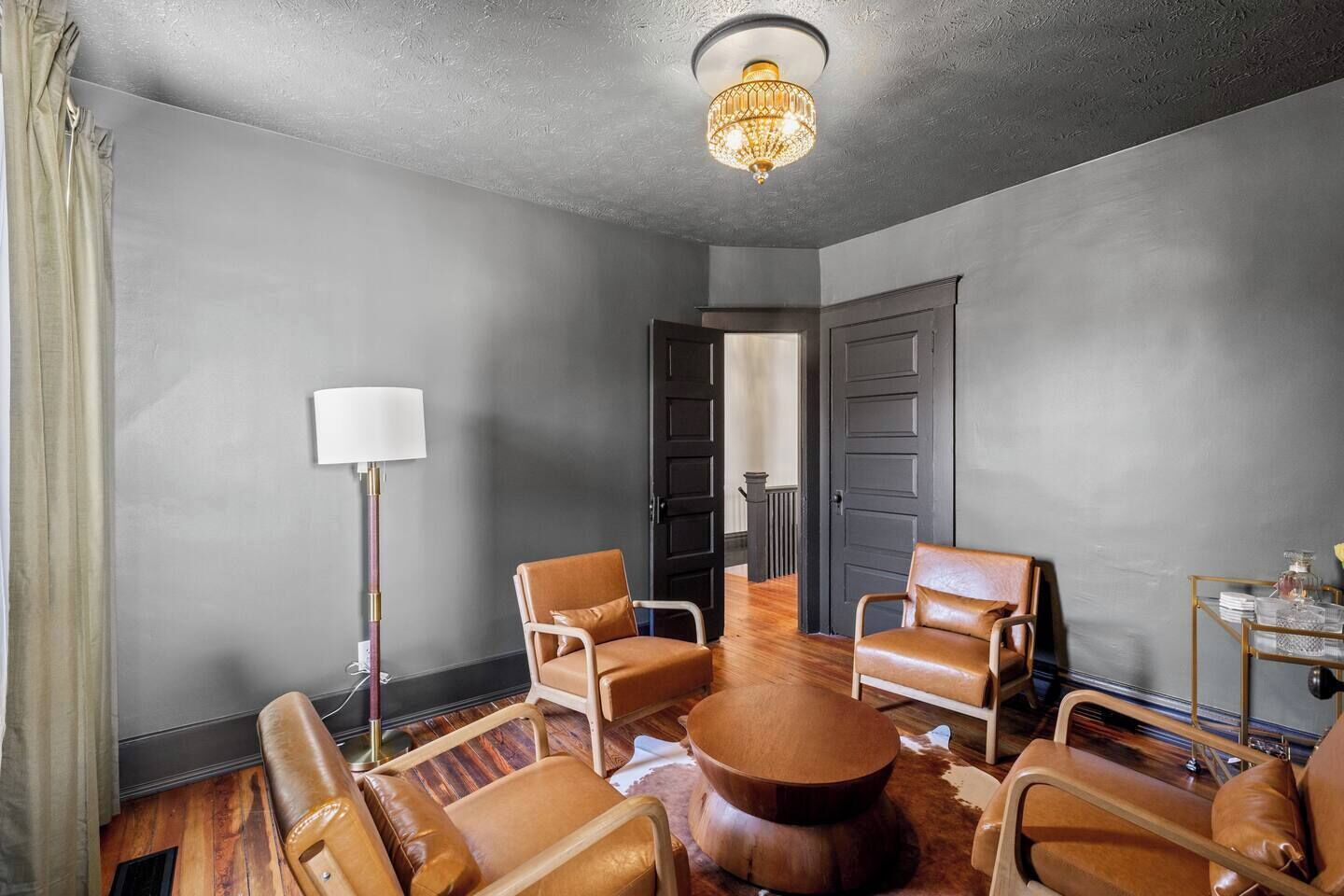 A conference room with leather chairs, a round wooden table, a floor lamp, and a chandelier.