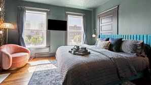 Une chambre à coucher comprenant un lit, une chaise, un téléviseur à écran plat et une fenêtre avec des rideaux.