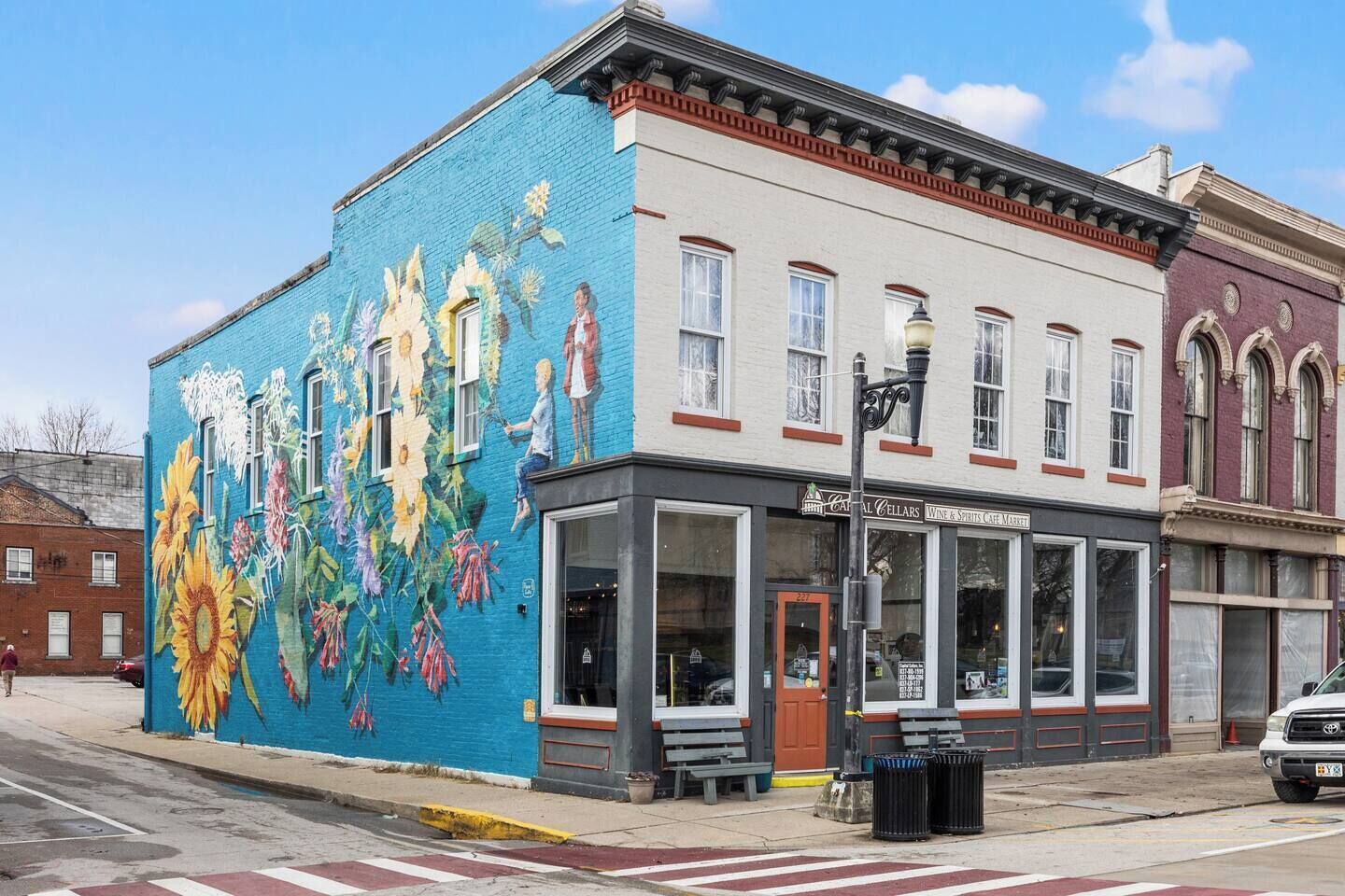A building with a colorful mural on the side, a storefront with large windows, and a street corner with a crosswalk.