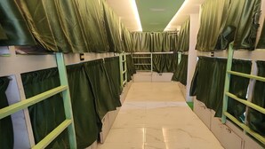 A corridor with bunk beds, each with green curtains, and a marble-tiled floor. - Nest Stays Hostel (Mumbai)