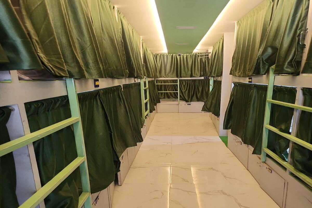 A corridor with bunk beds, each with green curtains, and a marble-tiled floor.