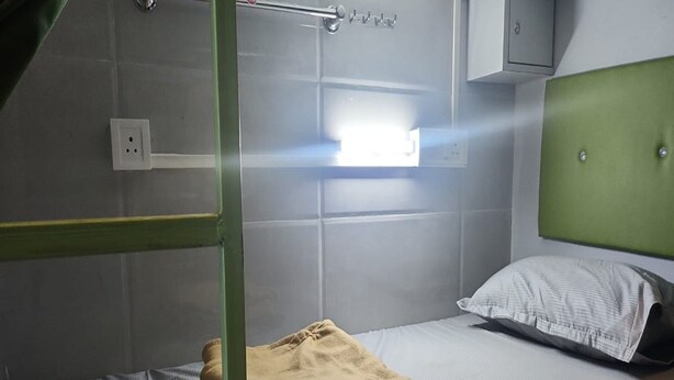 A bunk bed with a green headboard, a white pillow, and a yellow blanket. - Nest Stays Hostel (Mumbai)