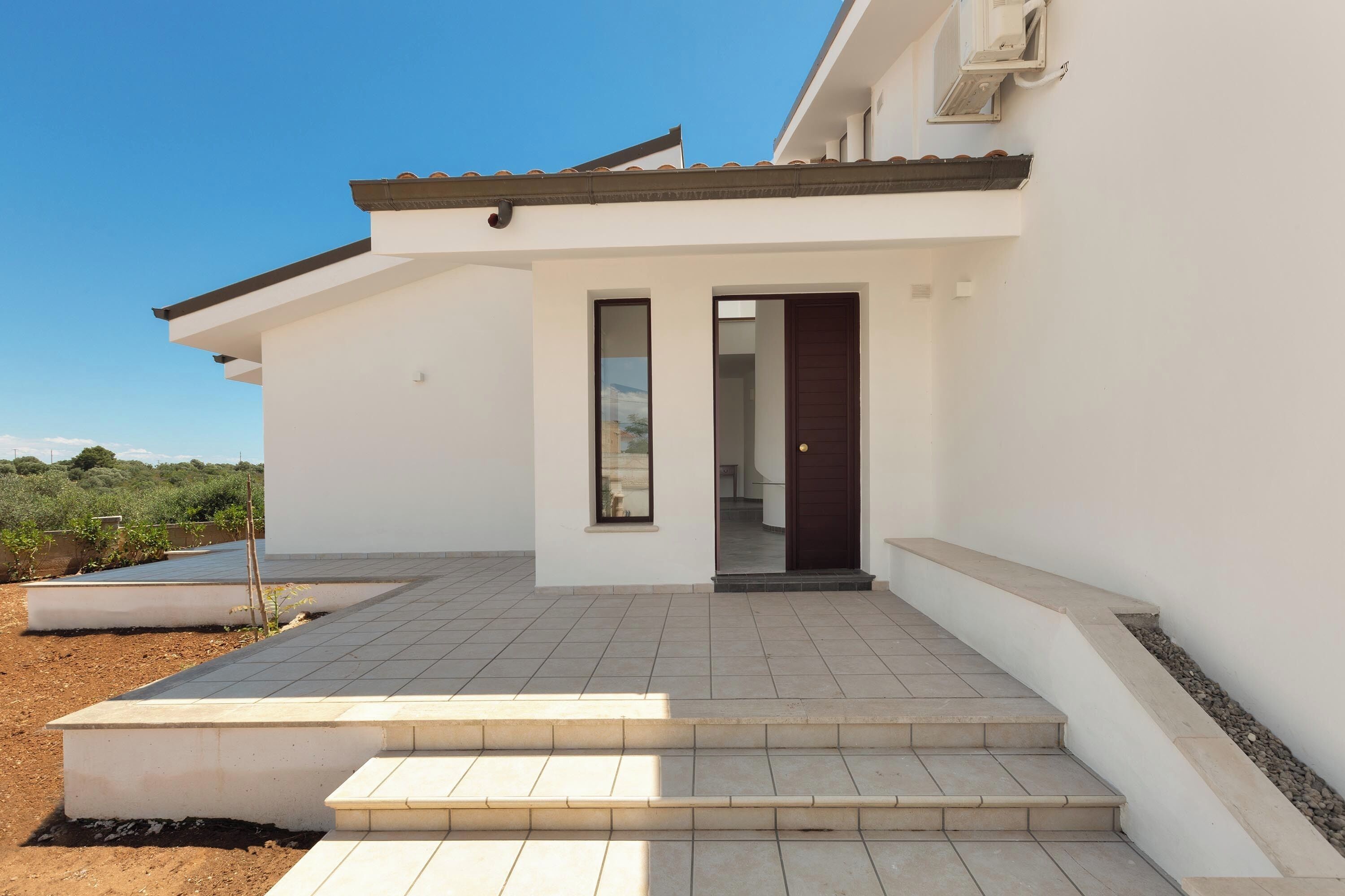 Una casa moderna con fachada blanca, un patio adoquinado y una puerta oscura.