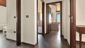 A hallway with a wooden door frame, a white wall, and a tiled floor.