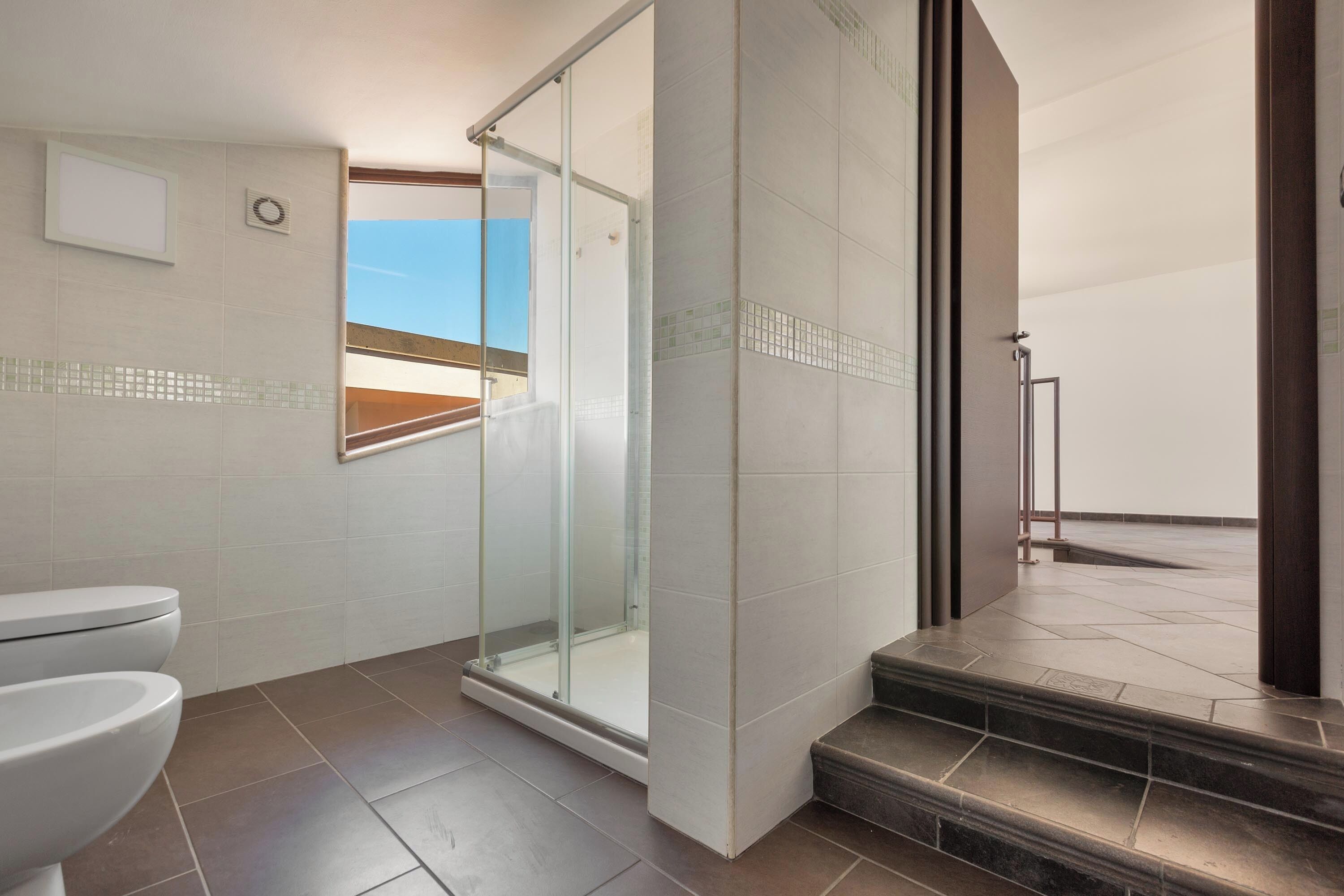 A modern bathroom with a glass shower enclosure, a toilet, and a view of the sky through a window.