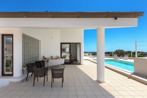 Un espacio exterior techado con piscina, sillones de descanso y una mesa con sillas.