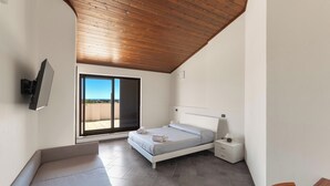 A bedroom with a bed, a nightstand, a TV mounted on the wall, and a sliding glass door leading to a balcony.