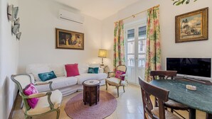 Un salon avec un canapé blanc, des fauteuils verts et blancs, une table à manger et un téléviseur.