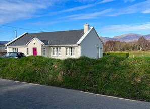 Stunning two-story house with a red door, surrounded by lush greenery and rolling hills.