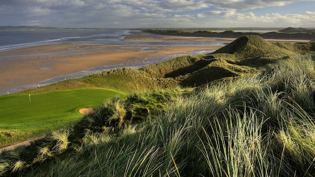 Un paisaje costero con un campo de golf, una playa y dunas.