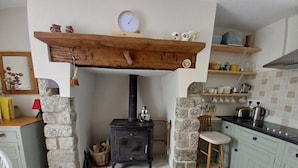 Una cocina rústica con estufa de leña, paredes de piedra y techo con vigas de madera.