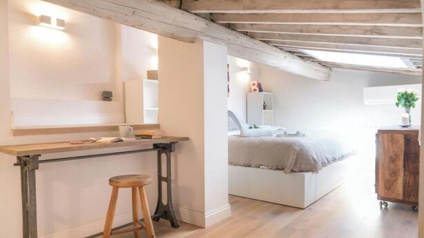 A bedroom with a bed, bedside table, and a small stool.