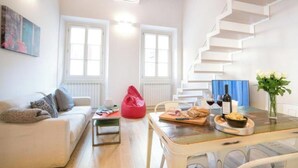 A modern living room with a staircase, a dining table with food and drinks, a red bean bag, and a painting on the wall.