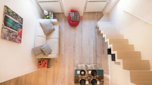 A modern apartment with a staircase, a red bean bag chair, a white sofa, and a coffee table with speakers.