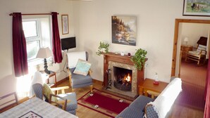 A cozy living room with a fireplace, comfortable seating, a dining table, and a television. - Bridies Holiday Cottage Roundstone (Inishnee)