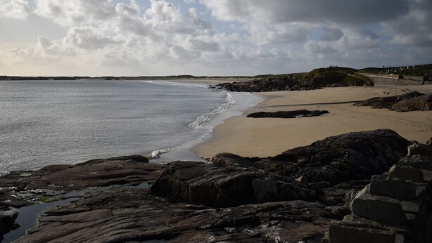 A coastal landscape with a sandy beach, rocky foreground, and a distant shoreline. - Bridies Holiday Cottage Roundstone (Inishnee)