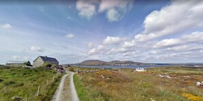 A rural landscape with a gravel path leading to a stone house with a metal roof. - Bridies Holiday Cottage Roundstone (Inishnee)